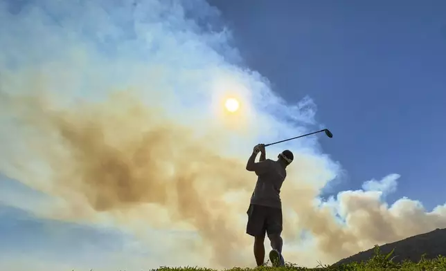 Smoke rises from the Airport Fire as Cizar Moon works out at the driving range at Eagle Glen Golf Club in Corona, Calif., on Tuesday, Sept. 10, 2024. (Jeff Gritchen/The Orange County Register via AP)