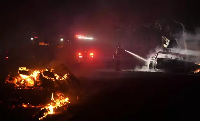 A firefighter hoses down a vehicle after the Airport Fire swept through Tuesday, Sept. 10, 2024, in El Cariso, an unincorporated community in Riverside County, Calif. (AP Photo/Eric Thayer)