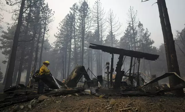 A firefighter hoses down hot spots on a fire-ravaged property while battling the Bridge Fire Wednesday, Sept. 11, 2024, in Wrightwood, Calif. (AP Photo/Eric Thayer)