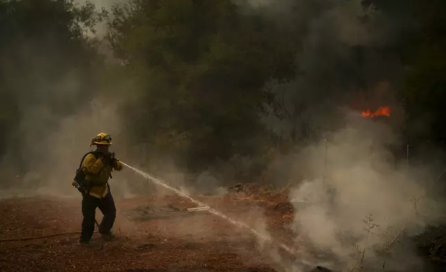 A firefighter sprays a hose to a smoldering property while battling the Airport Fire Tuesday, Sept. 10, 2024, in El Cariso, an unincorporated community in Riverside County, Calif. (AP Photo/Eric Thayer)