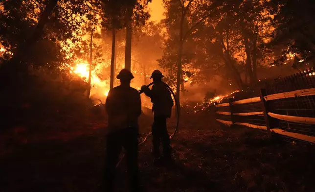 Two firefighters watch as the Bridge Fire burns near homes in Wrightwood, Calif., Tuesday, Sept. 10, 2024. (AP Photo/Jae C. Hong)