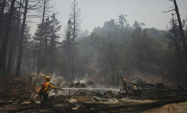 A firefighter hoses down hot spots on a fire-ravaged property while battling the Bridge Fire Wednesday, Sept. 11, 2024, in Wrightwood, Calif. (AP Photo/Eric Thayer)