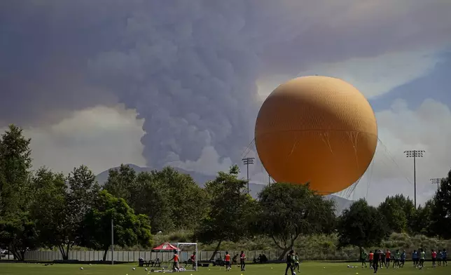 A plum of smoke created by the Airport Fire rises over a group playing soccer Tuesday, Sept. 10, 2024, in a view from Irvine, Calif. (AP Photo/Eugene Garcia)