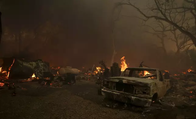 A destroyed car sits as structures burn after the Airport Fire swept through Tuesday, Sept. 10, 2024, in El Cariso, an unincorporated community in Riverside County, Calif. (AP Photo/Eric Thayer)