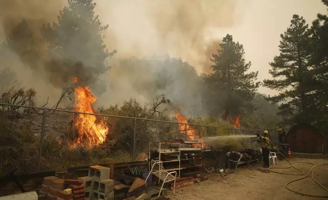 A firefighter douses flames in the perimeter of a property while battling the Bridge Fire Wednesday, Sept. 11, 2024, in Wrightwood, Calif. (AP Photo/Eric Thayer)