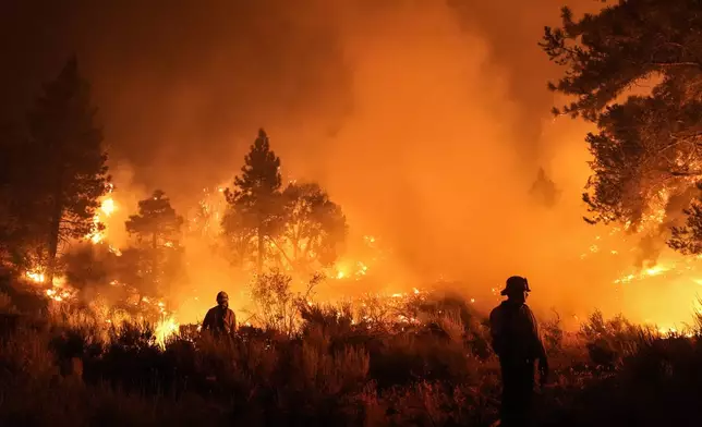 Two firefighters watch the Bridge Fire burn near a structure in Wrightwood, Calif., Tuesday, Sept. 10, 2024. (AP Photo/Jae C. Hong)