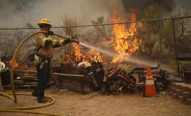 A firefighter douses flames in the perimeter of a property while battling the Bridge Fire Wednesday, Sept. 11, 2024, in Wrightwood, Calif. (AP Photo/Eric Thayer)