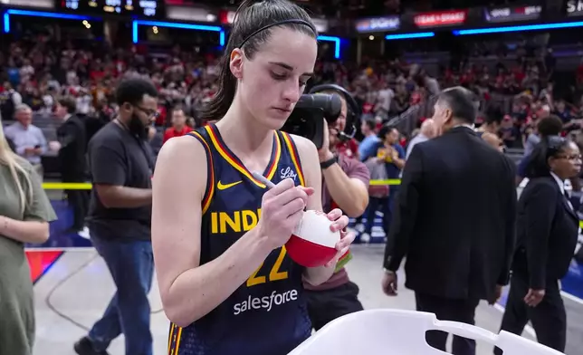 Indiana Fever guard Caitlin Clark (22) signs mini basketballs for fans following in a WNBA basketball game against the Dallas Wings in Indianapolis, Sunday, Sept. 15, 2024. (AP Photo/Michael Conroy)