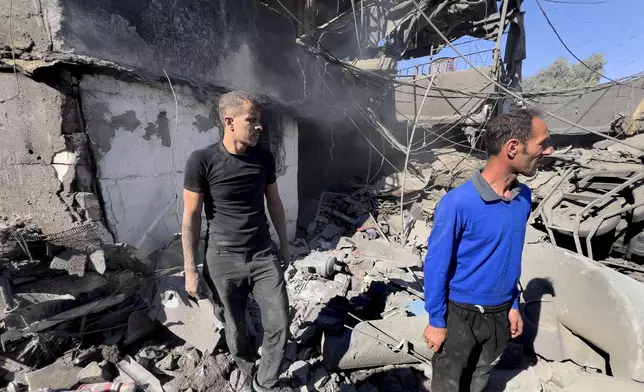 People stand on the rubble of a destroyed house at the site of Israeli airstrikes that targeted buildings facing the city's main government hospital in a densely-populated neighborhood, in southern Beirut, Lebanon, Tuesday, Oct. 22, 2024. (AP Photo/Hussein Malla)