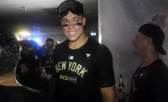 New York Yankees' Aaron Judge celebrates with teammates in the clubhouse following a 3-1 victory over the Kansas City Royals in Game 4 of an American League Division baseball playoff series Thursday, Oct. 10, 2024, in Kansas City, Mo. (AP Photo/Charlie Riedel)