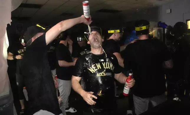 Members of the New York Yankees celebrate in the clubhouse following a 3-1 victory over the Kansas City Royals in Game 4 of an American League Division baseball playoff series Thursday, Oct. 10, 2024, in Kansas City, Mo. (AP Photo/Charlie Riedel)