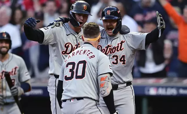 Detroit Tigers' Trey Sweeney (27) and Jake Rogers wait at home plate for teammate Kerry Carpenter (30) after Carpenter hit a three-run home run in the ninth inning during Game 2 of baseball's AL Division Series against the Cleveland Guardians, Monday, Oct. 7, 2024, in Cleveland. (AP Photo/David Dermer)