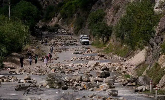 Pedestrians walk along a road blanketed with stones placed by supporters of Bolivian former President Evo Morales to prevent him from facing a criminal investigation over allegations of abuse of a minor and to demonstrate against an alleged assassination attempt, in Parotani, Bolivia, Tuesday, Oct. 29, 2024. (AP Photo/Juan Karita)