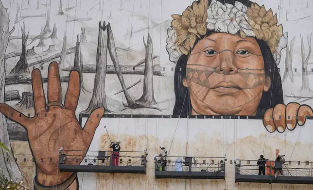 Workers finalize a mural by artist-activist Mundano depicting the drought in the Amazon rainforest using paint made from the ashes of wildfires in the Amazon and mud from the floods in southern Brazil, on the side of a building in Sao Paulo, Tuesday, Oct. 22, 2024. (AP Photo/Andre Penner)