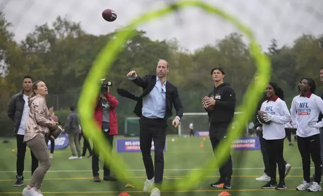 Britain's Prince William throws a football at a target, watched by Louis Rees-Zammit, left, as he attends a NFL Foundation NFL Flag event, an inclusive and fast paced American Football format, in London, Tuesday, Oct. 15, 2024. (AP Photo/Kin Cheung, Pool)