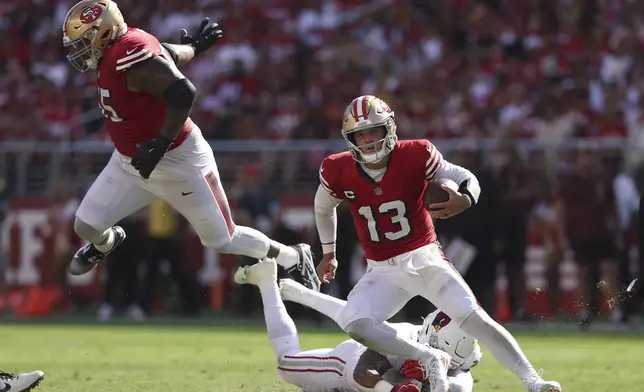 San Francisco 49ers quarterback Brock Purdy (13) runs in front of guard Aaron Banks, top, and Arizona Cardinals linebacker Kyzir White during the second half of an NFL football game in Santa Clara, Calif., Sunday, Oct. 6, 2024. (AP Photo/Jed Jacobsohn)