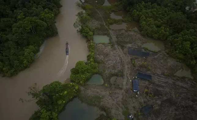 A boat, with gasoline to be taken to illegal mining machinery, maneuvers past an area that was mined and is being reforested by Asociacion Nuestra Casa Comun, or Our Community House Association, near Paimado, Colombia, Tuesday, Sept. 24, 2024. (AP Photo/Ivan Valencia)