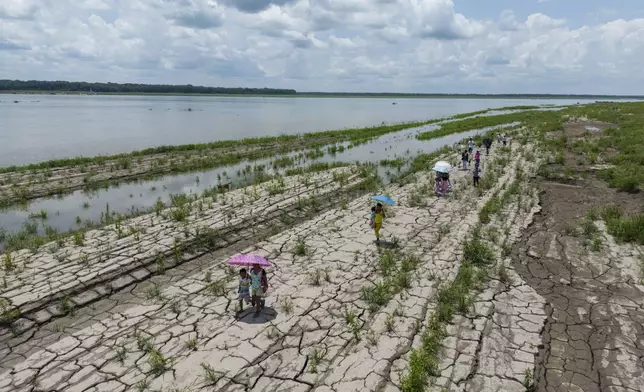 People walk through a part of the Amazon River that shows signs of drought in Santa Sofia, on the outskirts of Leticia, Colombia, Sunday, Oct. 20, 2024. (AP Photo/Ivan Valencia)