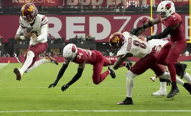 Washington Commanders quarterback Jayden Daniels, left, leaps into the end zone for a touchdown as Arizona Cardinals safety Jalen Thompson (34) defends during the second half of an NFL football game, Sunday, Sept. 29, 2024, in Glendale, Ariz. (AP Photo/Rick Scuteri)