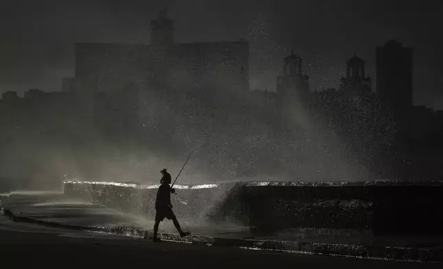 A person fishes along the boardwalk as waves crash in Havana, Monday, Oct. 21, 2024. (AP Photo/Ramon Espinosa)