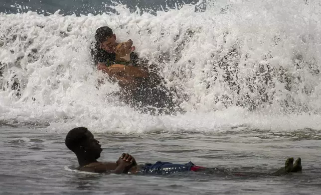 A man and his dog lean against the Malecon seawall as they play in the water crashing over it onto the sidewalk brought by Hurricane Milton passing through the Gulf of Mexico, in Havana, Cuba, Wednesday, Oct. 9, 2024. (AP Photo/Ramon Espinosa)