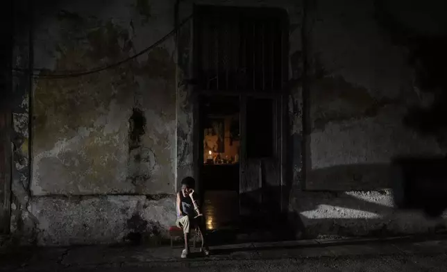 A resident sits while passing time during a blackout following the failure of a major power plant in Havana, Cuba, Saturday, Oct. 19, 2024. (AP Photo/Ramon Espinosa)