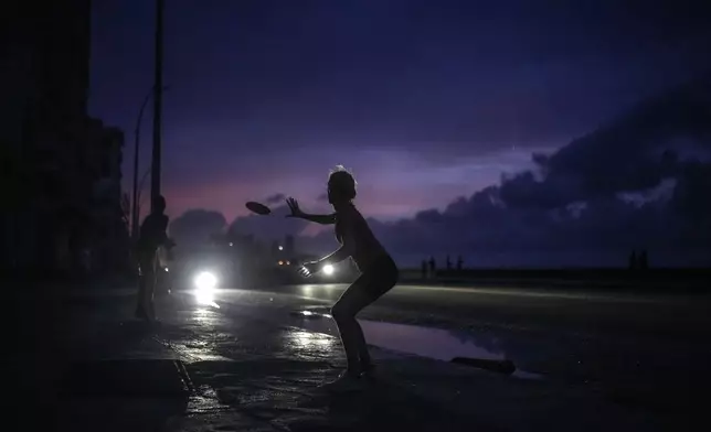 A woman prepares to catch a tossed frisbee during a massive blackout after a major power plant failed in Havana, Cuba, Friday, Oct. 18, 2024. (AP Photo/Ramon Espinosa)