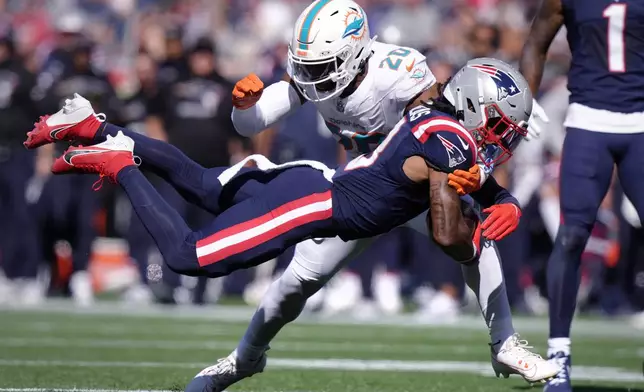 New England Patriots wide receiver DeMario Douglas hangs onto the ball as Miami Dolphins linebacker Jordyn Brooks (20) tries to block during the first half of an NFL football game, Sunday, Oct. 6, 2024, in Foxborough, Mass. (AP Photo/Steven Senne)