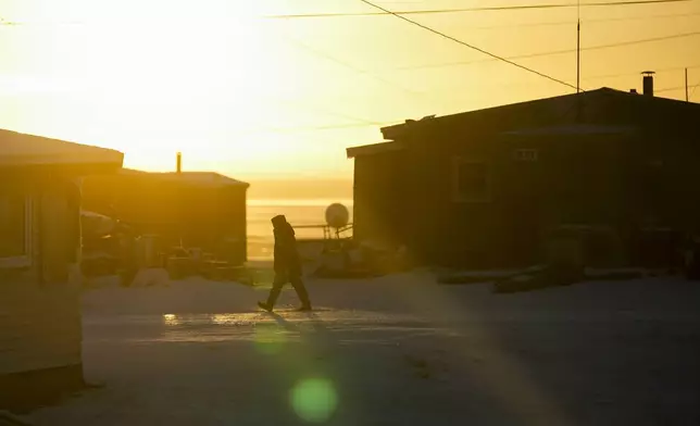 The sun rises over the village as a resident walks on a snowy road in Kaktovik, Alaska, Tuesday, Oct. 15, 2024. (AP Photo/Lindsey Wasson)