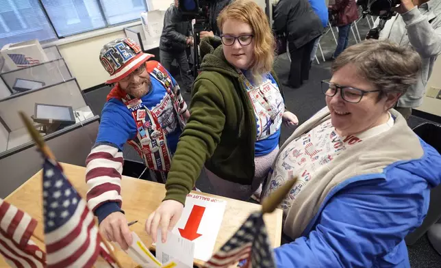 John Olsen, from left, his daughter Alice and his wife Ruby, of Ankeny, Iowa, cast their ballots during early voting at the Polk County Election Office, Wednesday, Oct. 16, 2024, in Des Moines, Iowa. (AP Photo/Charlie Neibergall)