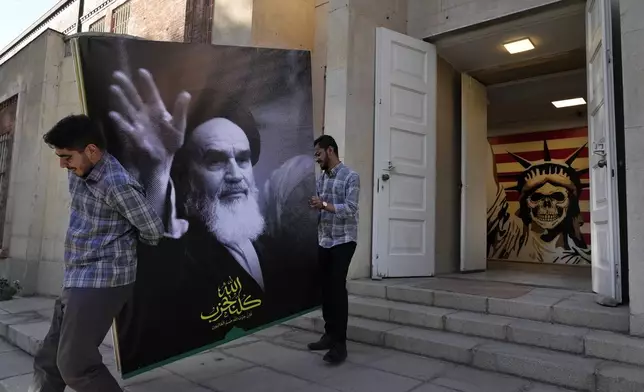 Two men carry a banner of the late Iranian revolutionary founder Ayatollah Khomeini at the entrance of the former U.S. Embassy, which has been turned into an anti-American museum, in Tehran, Iran, Tuesday, Oct. 22, 2024. (AP Photo/Vahid Salemi)