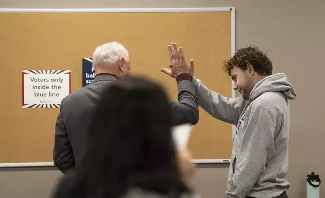 Democratic vice presidential nominee Minnesota Gov. Tim Walz, left, high-fives his son, Gus Walz, a first-time voter, as they cast their ballots during early voting at the Ramsey County Elections office in St. Paul, Minn., Wednesday, Oct. 23, 2024. (Renée Jones Schneider/Star Tribune via AP, Pool)