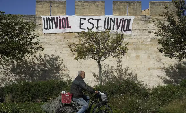 A man rides a bicycle in front of a banner reading: "A rape is a rape," in Avignon, southern France, Wednesday, Oct. 16, 2024. (AP Photo/Lewis Joly)