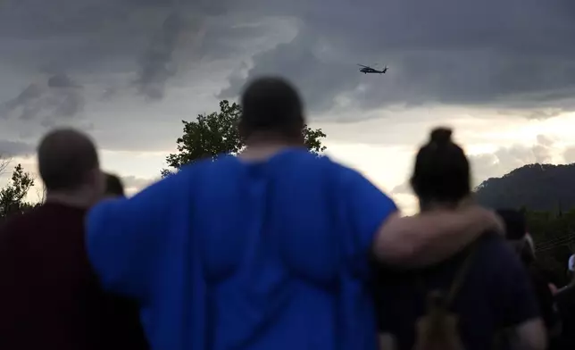 Mourners gather during a vigil for victims of the Impact Plastics tragedy as a helicopter continues search and rescue work over the disaster site in the distance in the days after Hurricane Helene in Erwin, Tenn., on Thursday, Oct. 3, 2024. (AP Photo/Jeff Roberson)