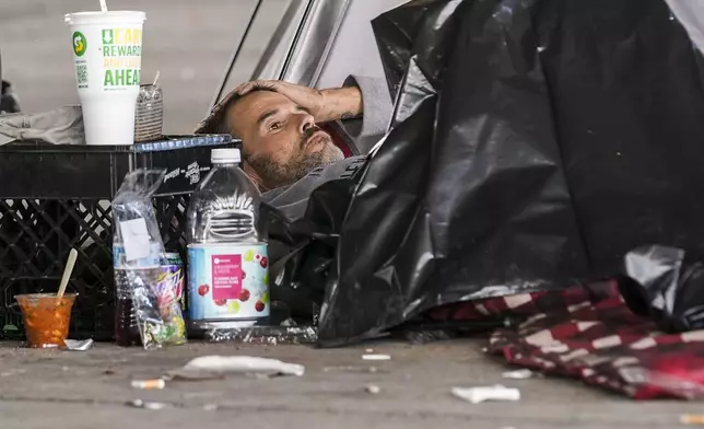 A man in a homeless encampment lays among possessions after Louisiana State police gave instructions for them to move to a different pre-designated location as they perform a sweep in advance of a Taylor Swift concert in New Orleans, Wednesday, Oct. 23, 2024. (AP Photo/Gerald Herbert)