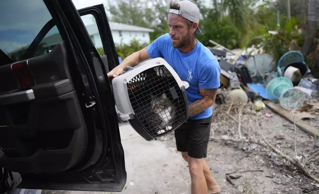 Ted Carlson puts his best friend Evan Purcell's cat McKenzie into a pick-up truck as the pair recover her along with other important items from Purcell's home ahead of the arrival of Hurricane Milton, as debris from Hurricane Helene damage to Purcell's garage level still sits alongside the driveway, in Holmes Beach on Anna Maria Island, Fla., Tuesday, Oct. 8, 2024. "This place couldn't handle Helene," said Carlson, predicting. "It's all going to be gone." (AP Photo/Rebecca Blackwell)