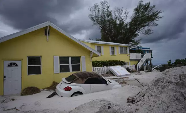 A car sits half-buried in sand as Bradenton Beach, Fla., which was in the process of cleaning up after Hurricane Helene, as Hurricane Milton approaches on Anna Maria Island, Tuesday, Oct. 8, 2024. (AP Photo/Rebecca Blackwell)