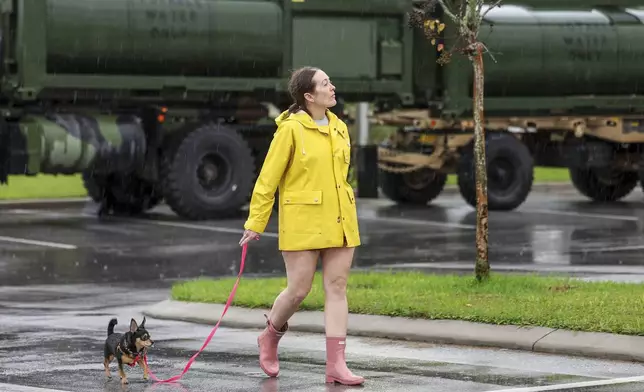 Erin Ferguson walks her dog while looking at equipment stationed by the Florida National Guard in preparation for Hurricane Milton in New Port Richey, Fla., Wednesday, Oct. 9, 2024. (AP Photo/Mike Carlson)