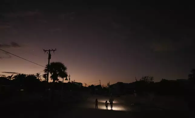 A family who went to check on their storm-damaged home uses flashlights to walk back up a sand-coated street, currently open only to pedestrians and vehicles involved in the recovery effort, on Manasota Key, Fla., as night falls, Saturday, Oct. 12, 2024. (AP Photo/Rebecca Blackwell)