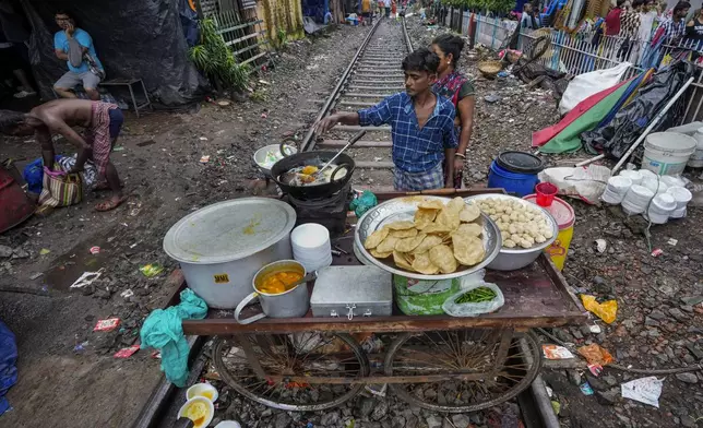 A vendor prepares breakfast on his mobile cart place on a railway track on which train services are suspended temporarily due to festival rush in Kolkata, India, Wednesday, Oct. 2, 2024. (AP Photo/Bikas Das)