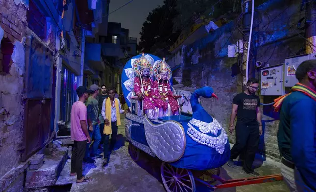 Indian artists dressed as Hindu deities Rama, left, and Lakshman, right, sit on a chariot being pulled by laborer that passes through the narrow alleys ahead of a religious procession during the Dussehra festival also known as Vijayadashami, the day Rama killed demon king Ravana who had abducted Rama's wife Sita, celebrating the victory of good over evil on 12th october in Prayagraj in the northern Indian state of Uttar Pradesh, India, Wednesday, Oct. 9, 2024. (AP Photo/Rajesh Kumar Singh)