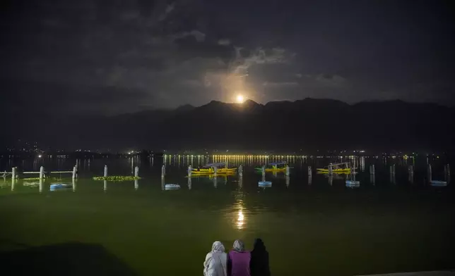 Kashmiri women watch a supermoon rising behind the Zabarwan hills as boatmen row their boats at the Dal Lake on the outskirts of Srinagar, Indian controlled Kashmir, Thursday, Oct. 17, 2024. (AP Photo/Mukhtar Khan)