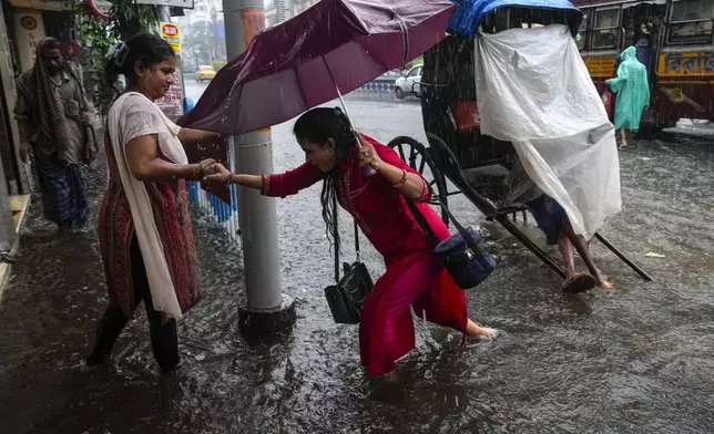 A woman helps another to wade through a waterlogged road during heavy rain following tropical storm Dana, in Kolkata, India, Friday, Oct. 25, 2024. (AP Photo/Bikas Das)