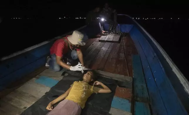 A paramedic examines the health condition of young girl as she lies on the deck of a boat carrying Rohingya Muslims in the waters near the coast of Labuhan Haji, Aceh province, Indonesia, Tuesday, Oct. 22, 2024. (AP Photo/Binsar Bakkara)