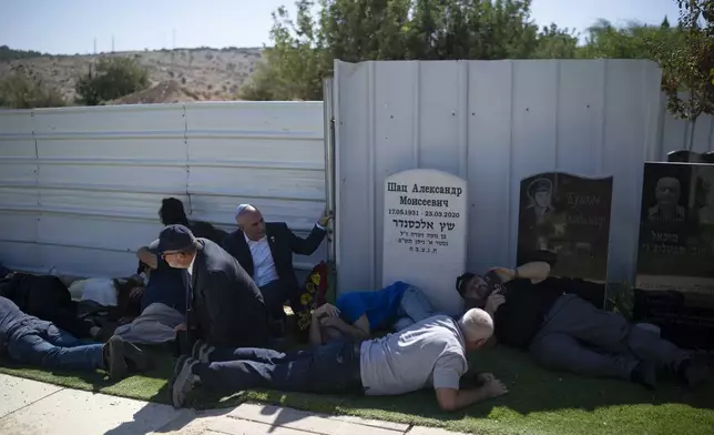 People take cover as a siren warns of incoming rockets during the funeral of Alexei Popov, who was killed during a rocket attack fired from Lebanon last weekend, at the Tel Regev cemetery in the outskirts of Haifa, northern Israel, Monday, Oct. 21, 2024. (AP Photo/Leo Correa)