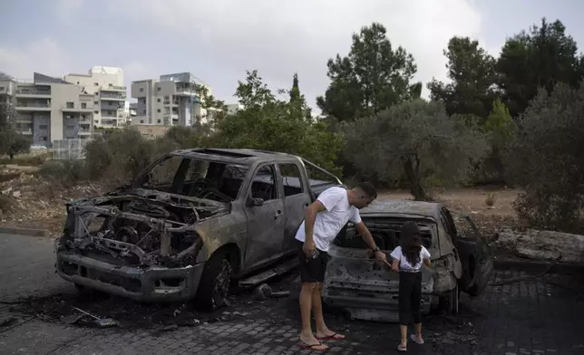 A man shows a burnt car to a girl, after a rocket launched from Lebanon, hit an area in Kfar Vradim, northern Israel, Monday, Oct. 7, 2024. (AP Photo/Leo Correa)