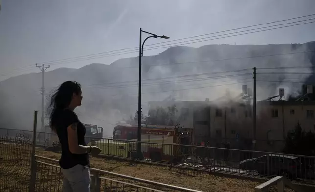 A woman looks on as firefighters work to extinguish a fire after a rocket, fired from Lebanon, hit a residential building in Kiryat Shmona, northern Israel, Wednesday, Oct. 9, 2024. (AP Photo/Leo Correa)