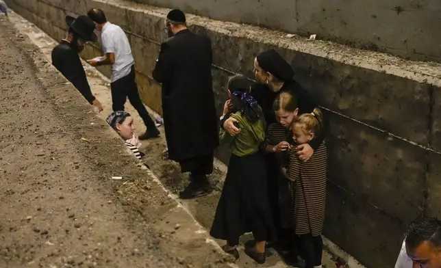 People take cover on the side of the road as a siren sounds a warning of incoming missiles fired from Iran on a freeway in Shoresh, between Jerusalem and Tel Aviv in Israel Tuesday, Oct. 1, 2024.(AP Photo/Ohad Zwigenberg)