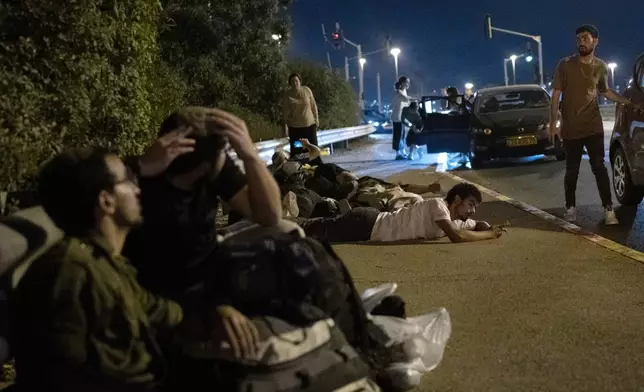 Israelis take cover as projectiles launched from Iran are being intercepted in the skies over in Rosh HaAyin, Israel, Tuesday, Oct. 1, 2024. (AP Photo/Maya Alleruzzo)