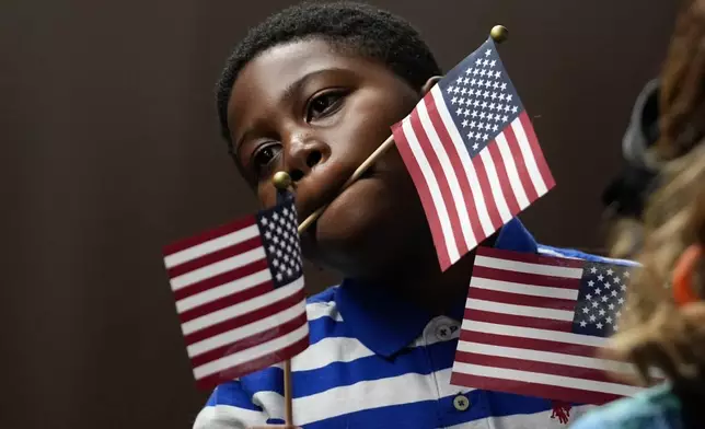 A young boy watches as people take the oath to become American citizens during a naturalization ceremony at the high school attended by former President Jimmy Carter Tuesday, Oct. 1, 2024, in Plains, Ga. (AP Photo/John Bazemore)